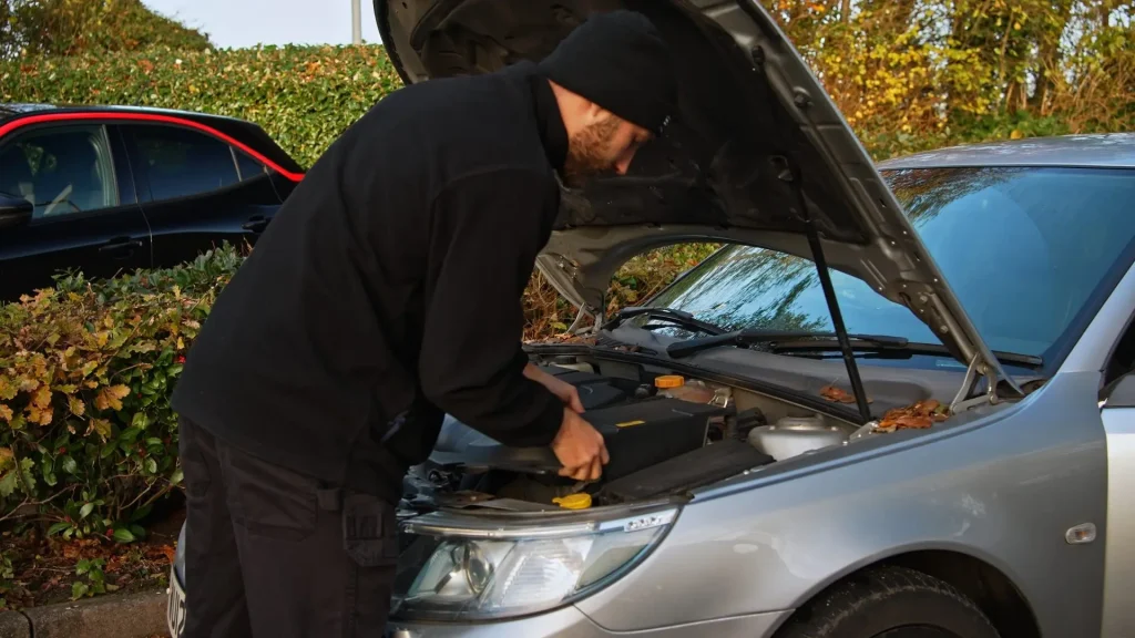 Technician at the open bonnet of a car outdoors