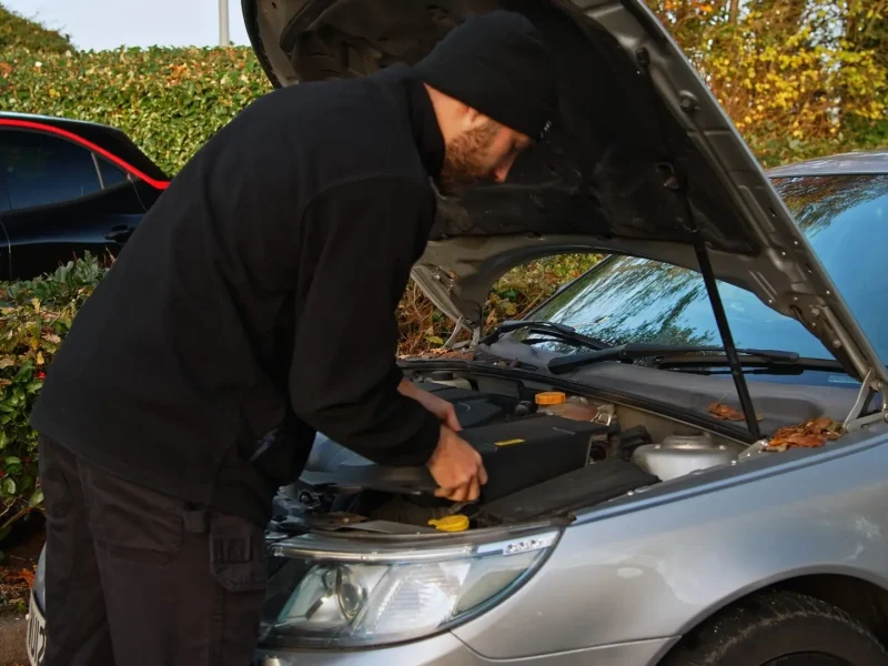 Technician at the open bonnet of a car outdoors